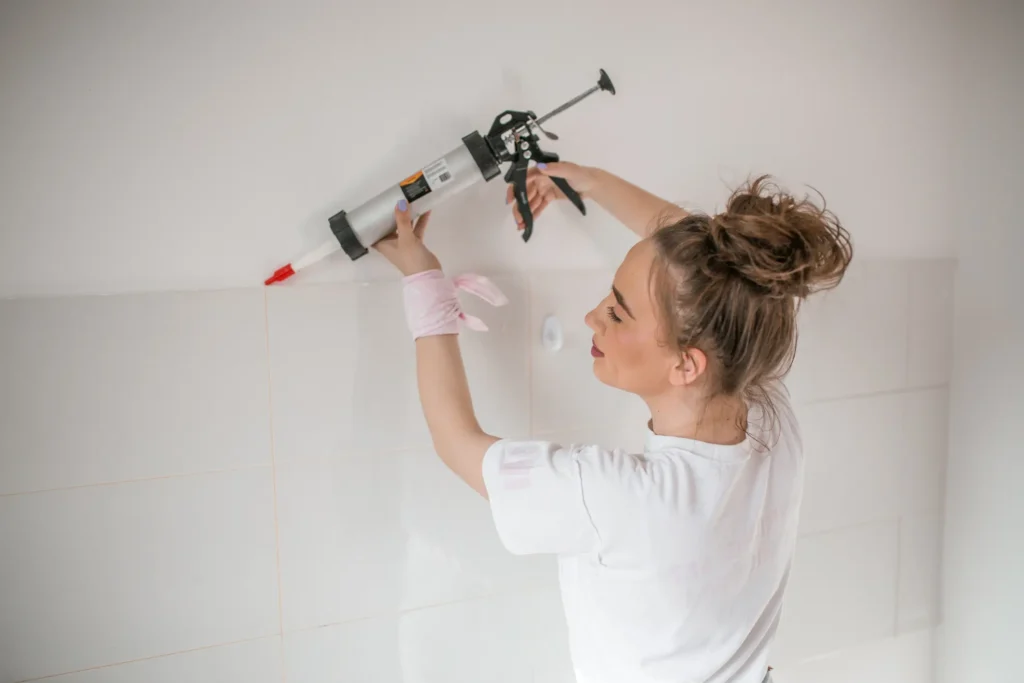 Woman applying silicone sealant with caulking gun on the wall